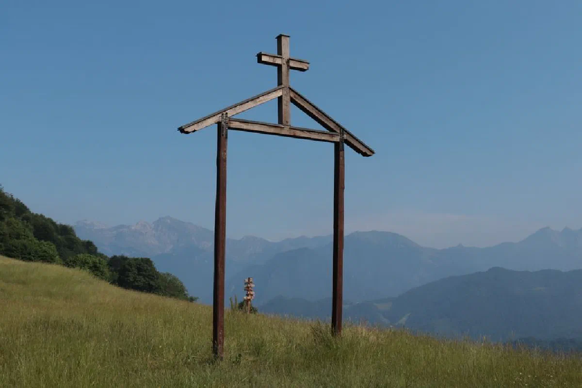 Rustic wooden cross on a grassy hill with scenic mountain view in Piemonte, Italy.